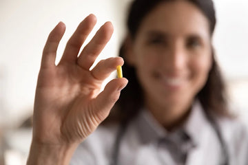 Woman holding a supplement tablet wearing a white coat with a stethoscope around her neck 